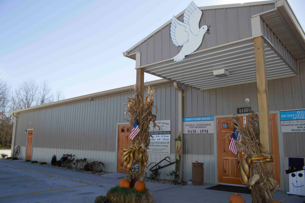 Community thrift store and food pantry entrance decorated with pumpkins, cornstalks, and American flags.