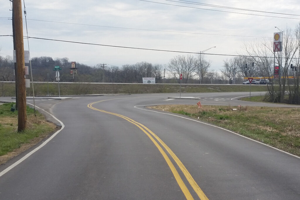 Newly paved curving road approaching an intersection with concrete traffic islands and yield signs.