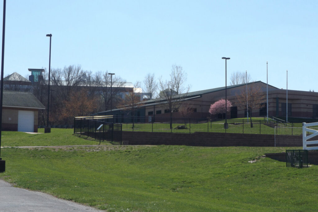 TASK athletic facility and fenced sports field surrounded by landscaped grassy grounds.