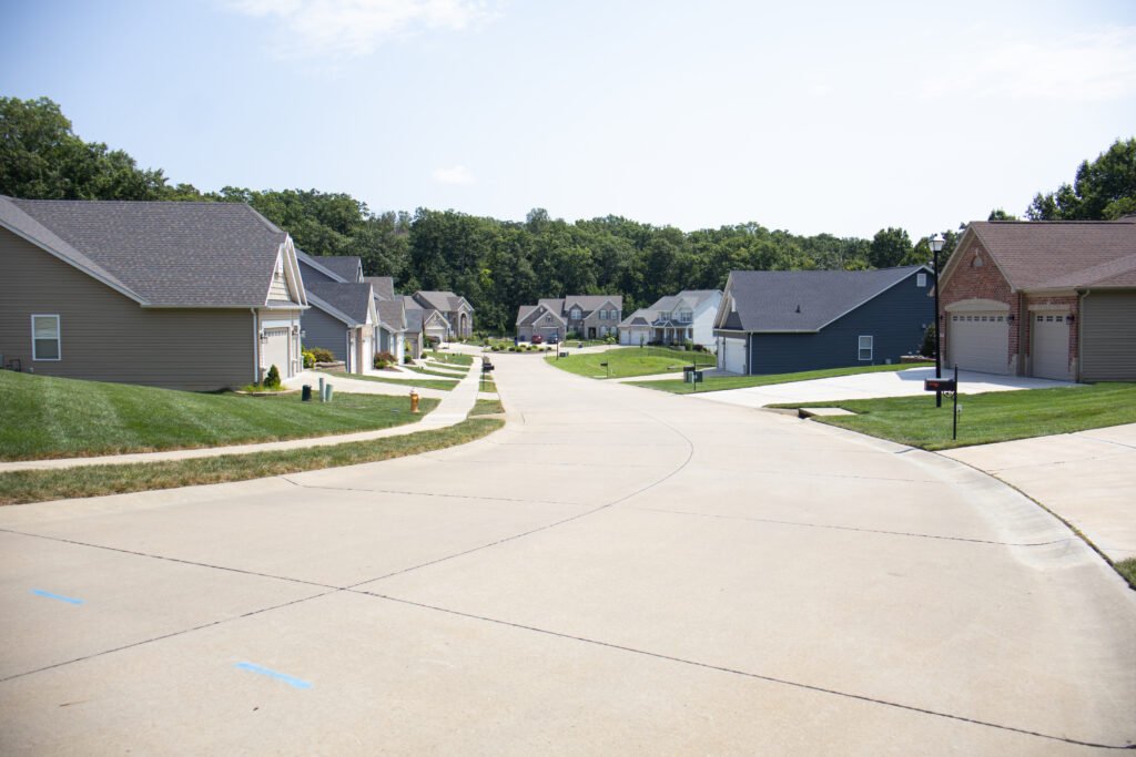 Suburban neighborhood with single-family homes, green lawns, and a curving residential street on a sunny day.