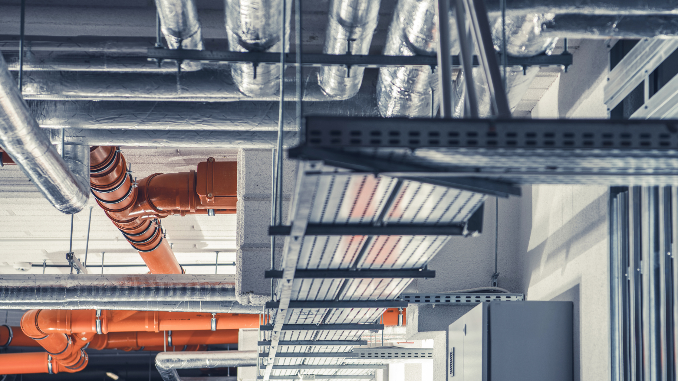Building interior with exposed mechanical piping, insulated ductwork, and suspended cable trays.