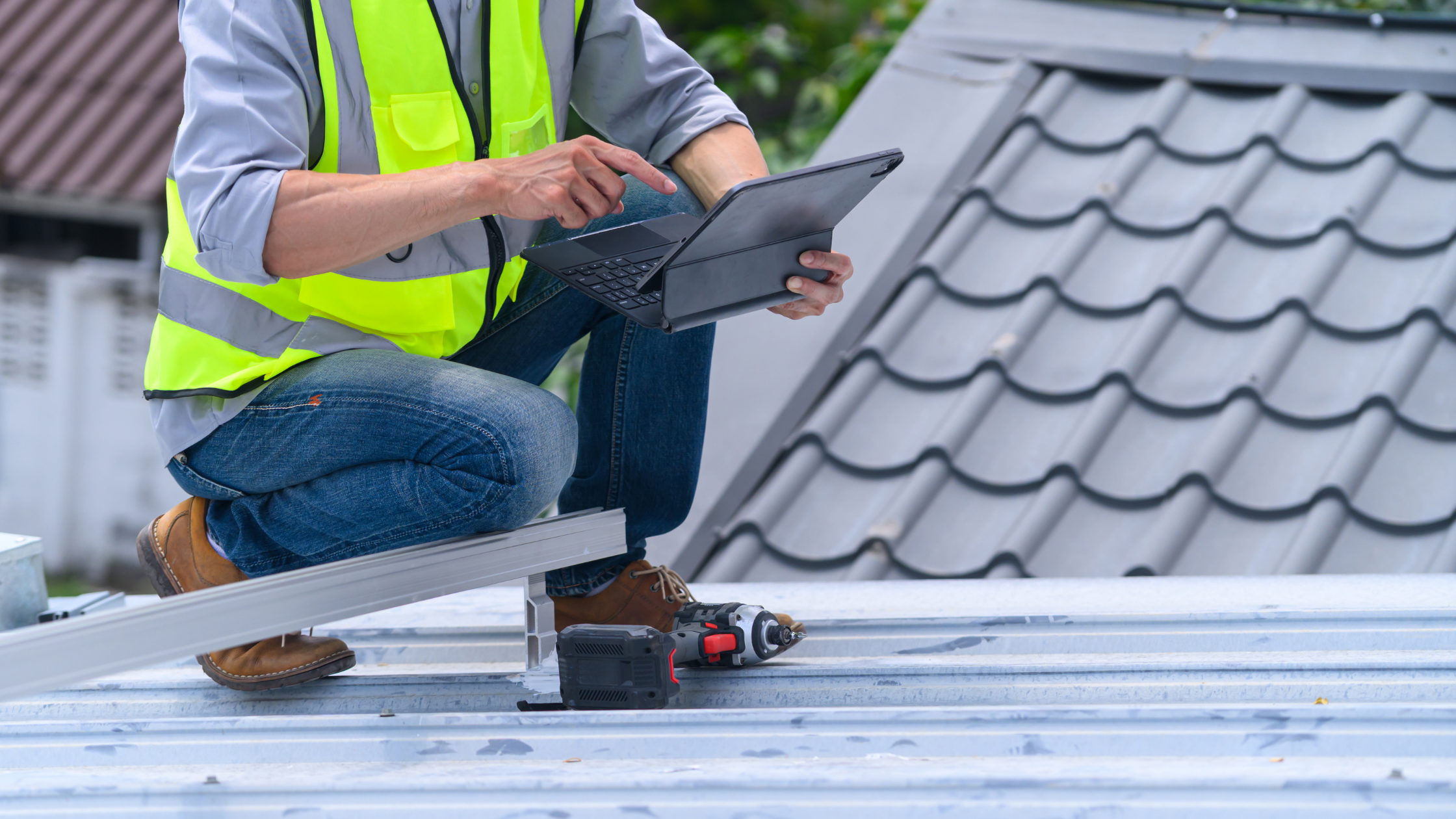 Construction professional in a safety vest using a tablet while inspecting a metal roof.