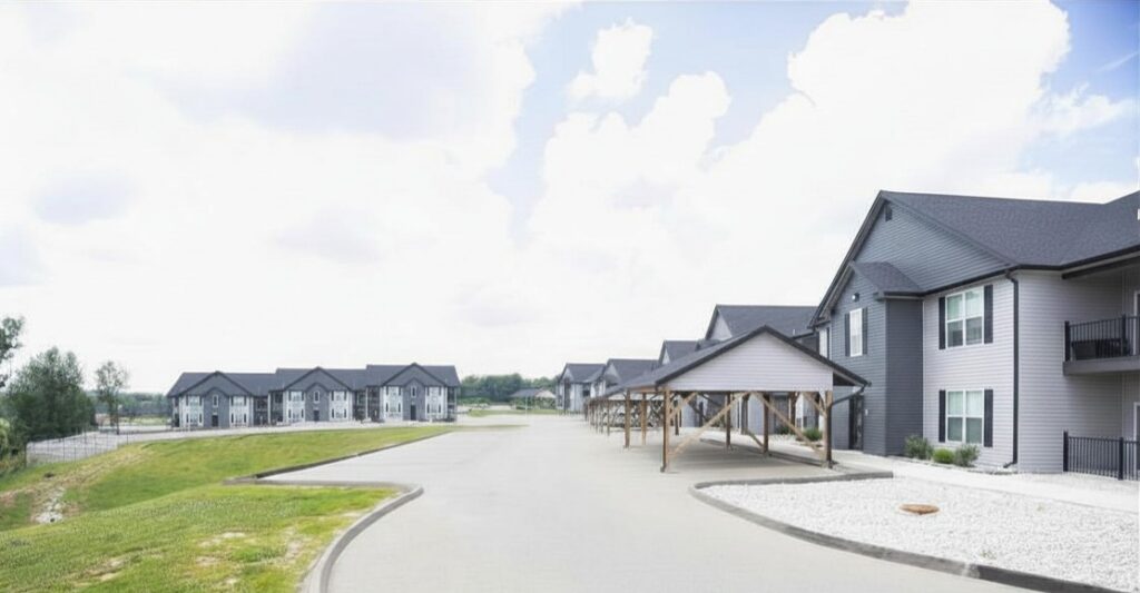 Modern apartment community with gray residential buildings, covered parking, and a paved access road.